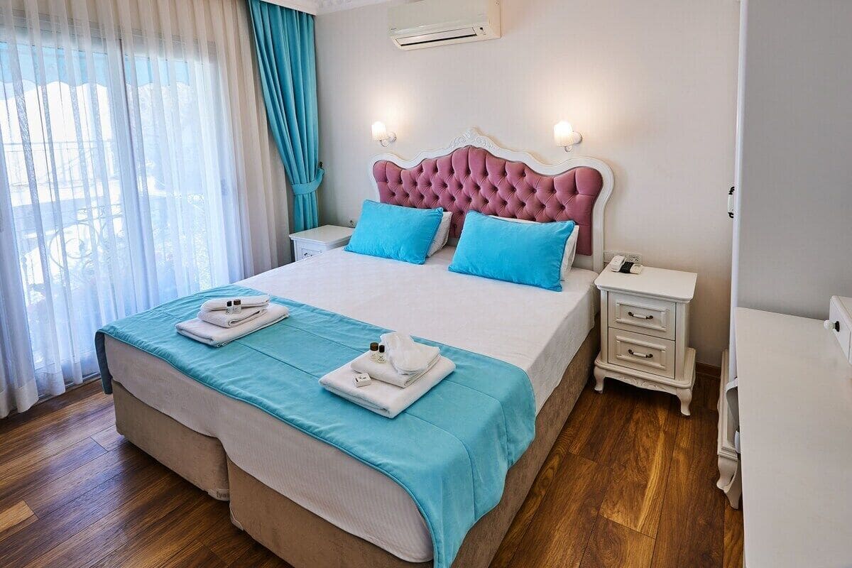A neatly made bed with a pink headboard, two bedside tables, and a window with curtains.