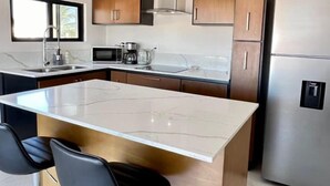 A modern kitchen with a central island, bar stools, stainless steel appliances, and wooden cabinets.