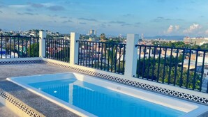 A rooftop swimming pool with a tiled border and a view of the cityscape in the background.