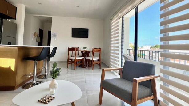 A modern living room with a dining area, a kitchen, and a balcony with a view.