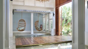 Un'area benessere con un pontile in legno sopra l'acqua, due poltrone in vimini e una ventola a soffitto.