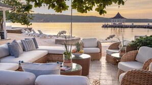 Zona relax sul mare con mobili in vimini, un divano bianco e vista sull'acqua.