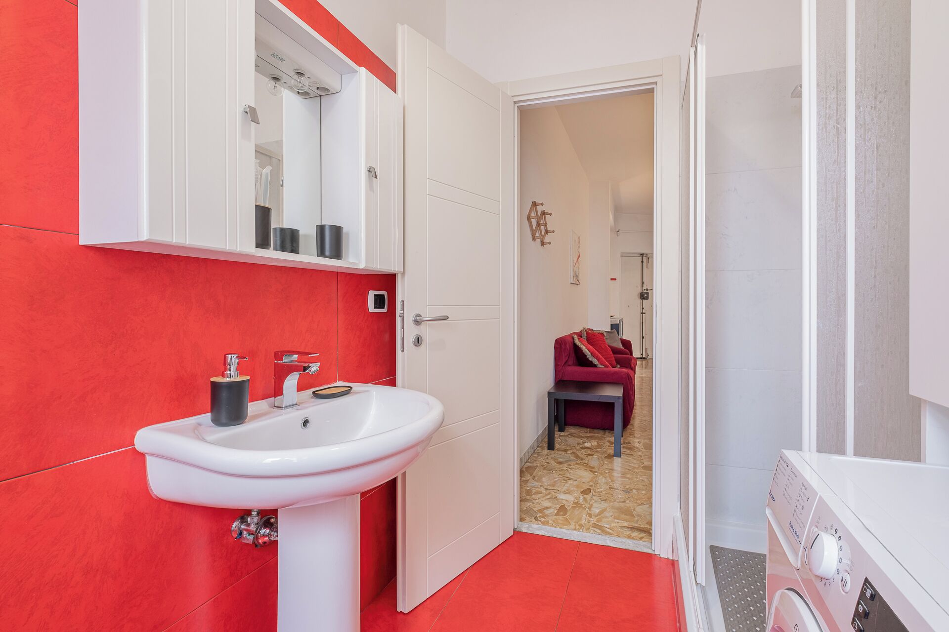 A bathroom with a white sink, red walls, and a door leading to a shower area.
