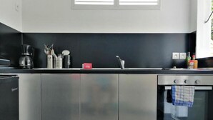 A modern kitchen with stainless steel appliances, a window above the sink, and a red sign on the countertop. - Résidence KAZ A Bibi - Flamboyant (Sainte-Rose)