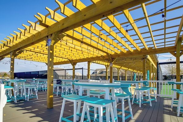 Une terrasse extérieure dotée d’une pergola en bois, de tables et de chaises blanches et turquoise.