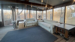 Una habitación acogedora con un ventanal grande, un sofá, un ventilador y una mesa.