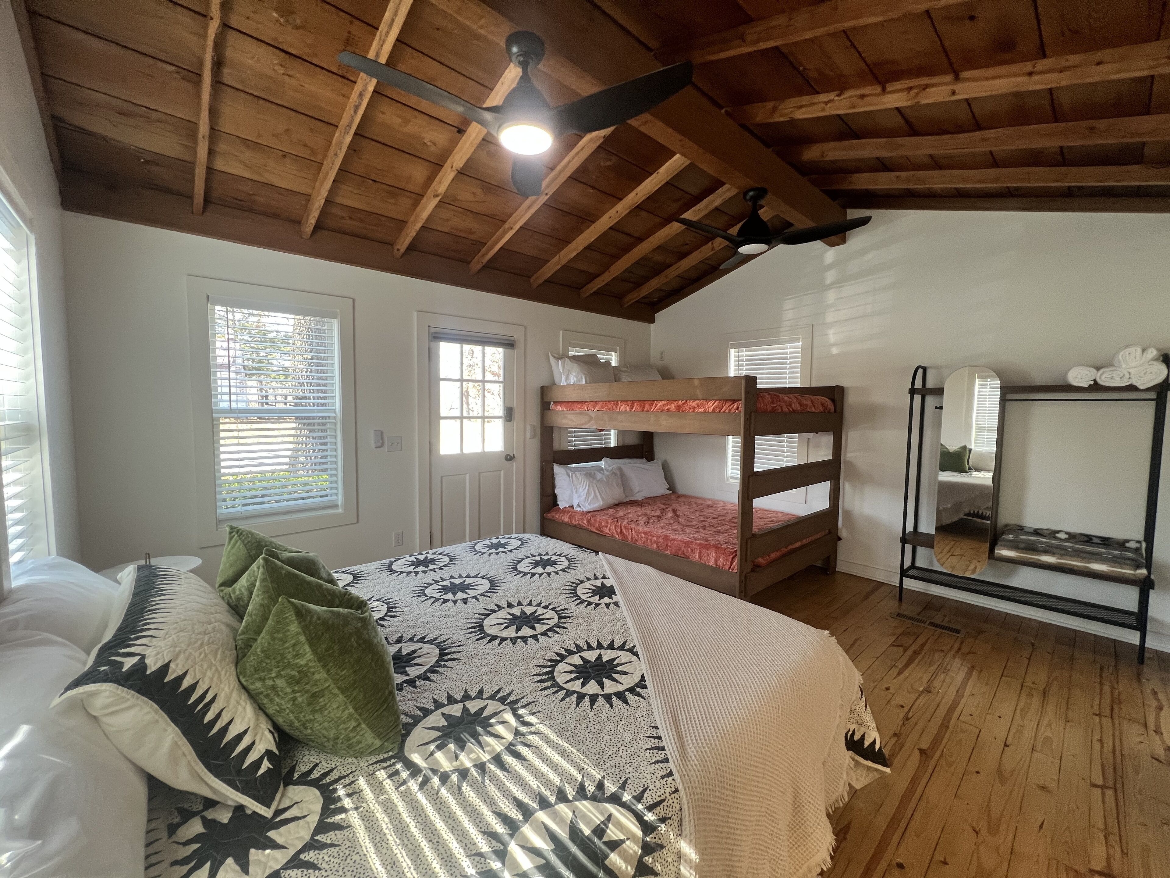 Une chambre avec un lit superposé, un lit simple, un ventilateur de plafond et une étagère avec des serviettes.