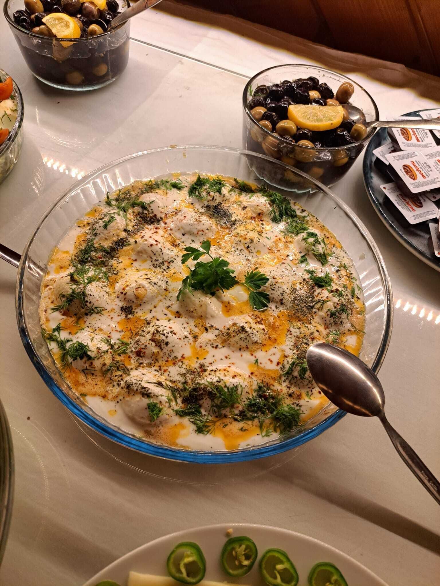 A bowl of food garnished with herbs and spices, surrounded by other dishes and condiments on a table.