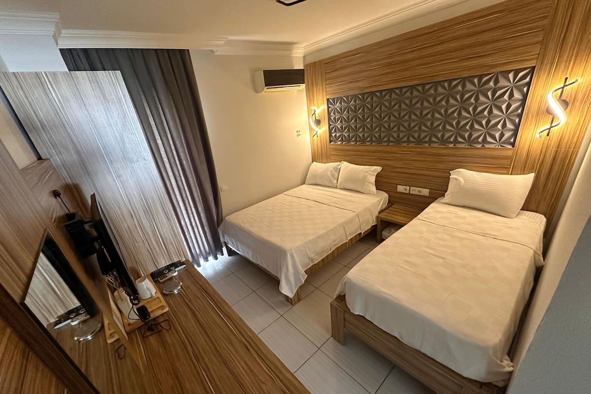 A hotel room with two beds, a wooden headboard, a mirror, a desk with a lamp, and a window with curtains.