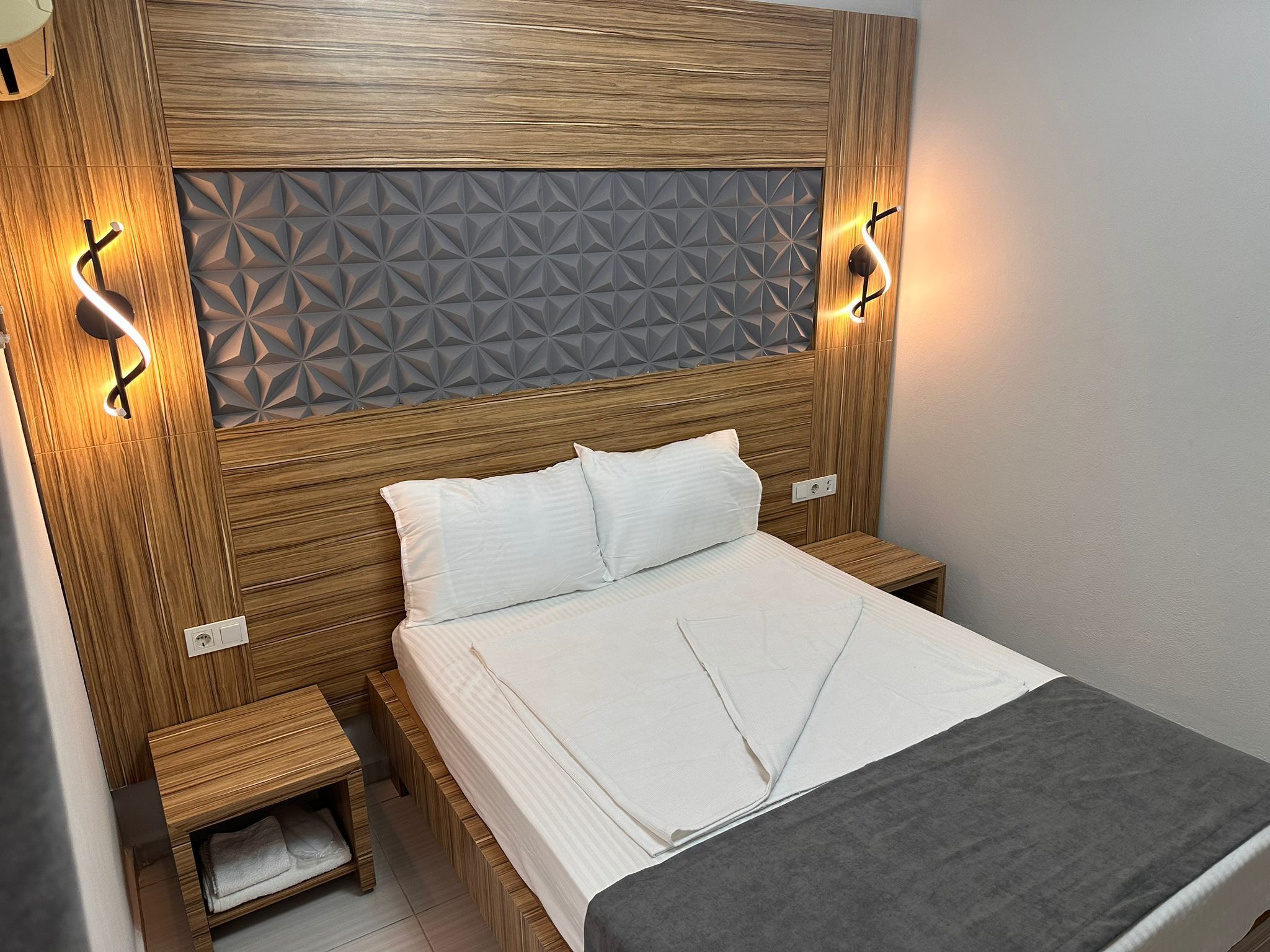A neatly arranged bedroom with a wooden headboard, a bed with white linens, and two bedside tables.