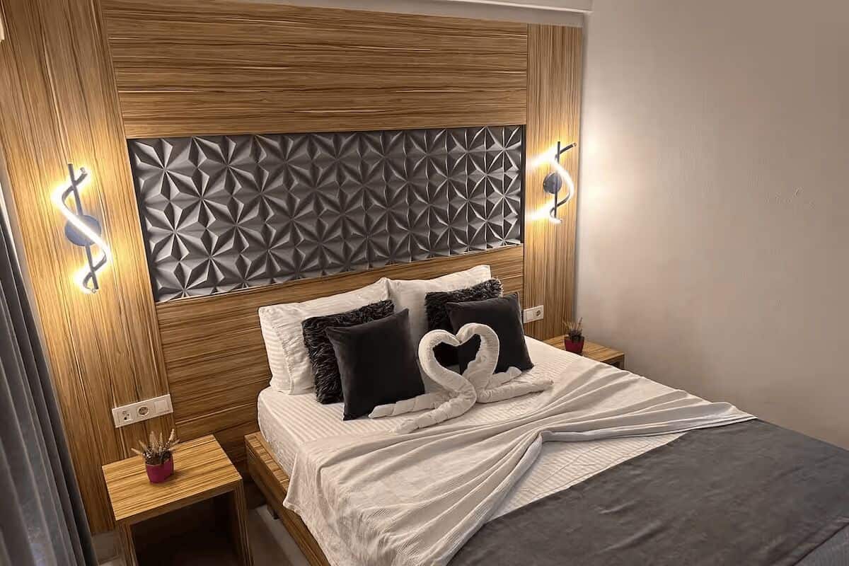 A neatly made bed with a heart-shaped pillow arrangement, wooden headboard with geometric paneling, and bedside lamps.