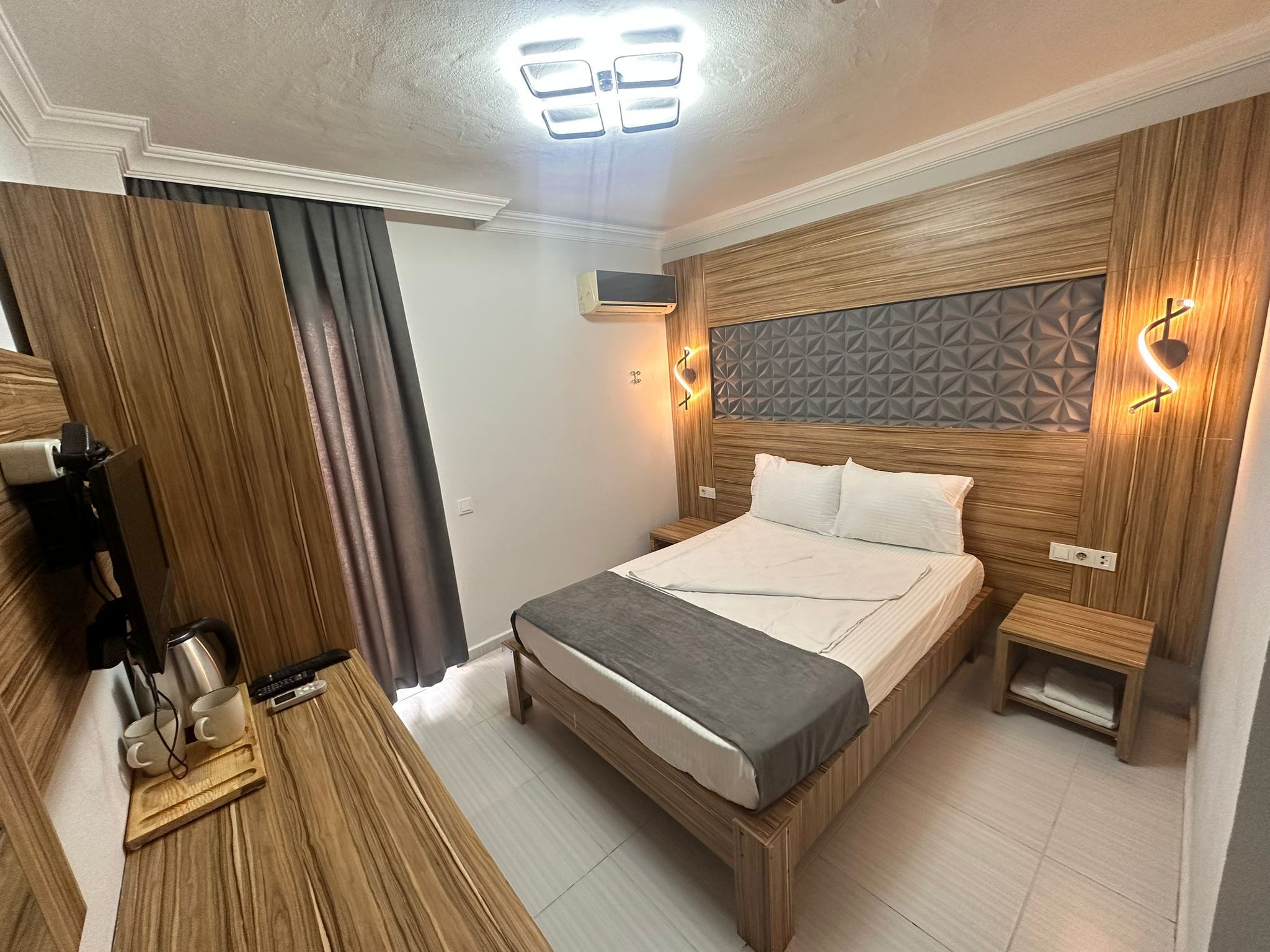 A modern bedroom with a wooden headboard, a bed with white linens, a bedside table, and a nightstand.