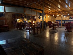 A rustic wooden interior with a dining area featuring wooden tables and chairs, a bar area with stools, and a large window providing natural light. - Royal Ezel Hotel (Antalya)