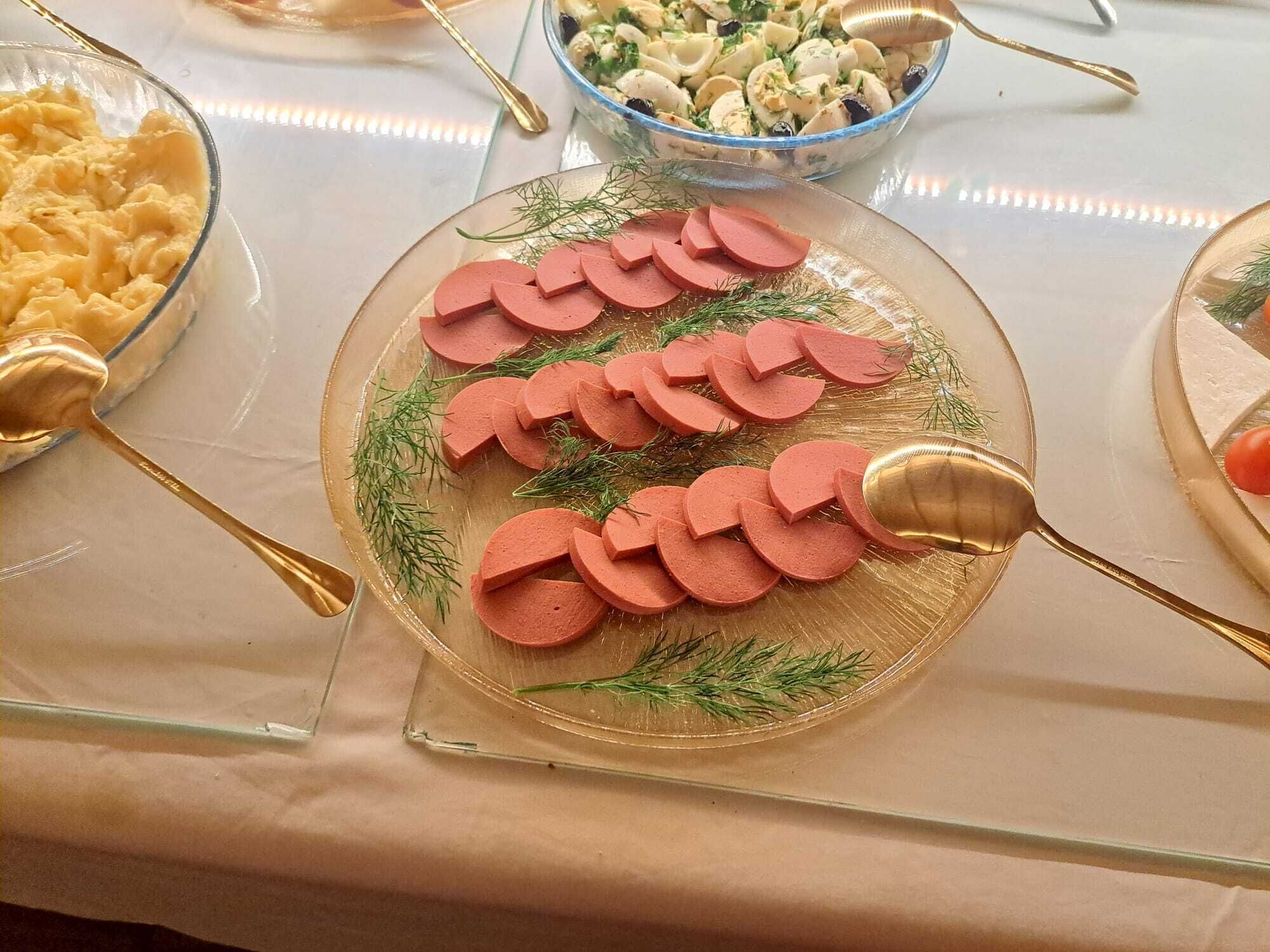 Una mesa de buffet con diversos platos, incluyendo un plato de salchicha en rodajas adornada con eneldo.