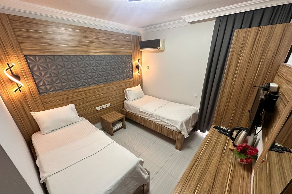 A hotel room with two beds, a small bedside table, a desk with a coffee machine, and a TV.