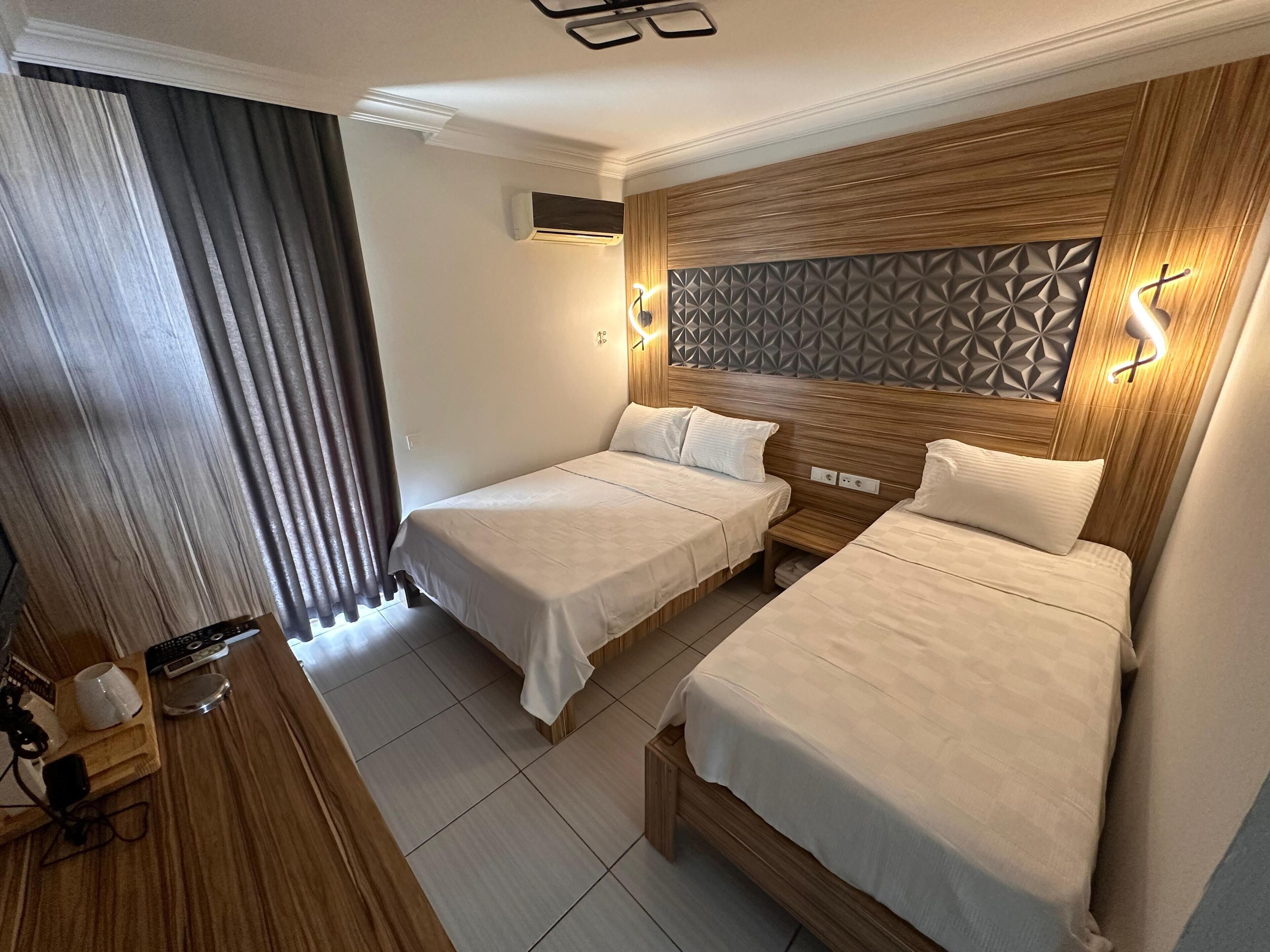 Una habitación de hotel con dos camas, un cabecero de madera, un aire acondicionado instalado en la pared y una mesita de noche con lámpara.