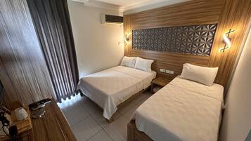 Une chambre d’hôtel avec deux lits, une tête de lit en bois, un climatiseur fixé au mur et une table de chevet avec une lampe.