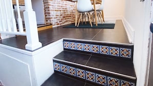 A staircase with patterned tiles leading to a dining area with a brick wall and a kitchen in the background.