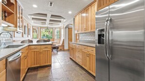 Una cocina moderna con armarios de madera, un refrigerador de acero inoxidable y un piso de baldosas de piedra.
