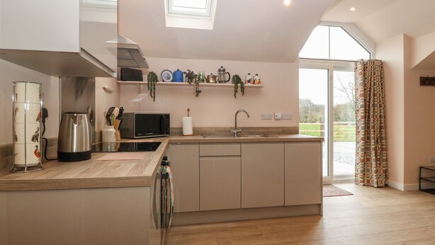 A modern kitchen with a central island, stainless steel appliances, and a large window. - Y Felin (Caernarfon)
