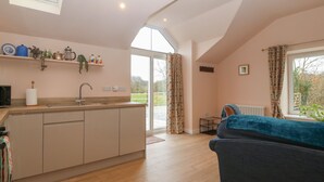 A modern kitchen with a large island, a dining area with a blue sofa, and a view of the outdoors through a large window. - Y Felin (Caernarfon)