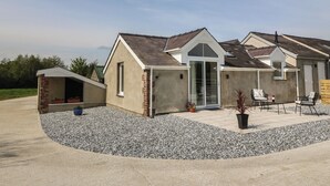 A single-story house with a covered porch, a garage, and a patio area with outdoor seating. - Y Felin (Caernarfon)