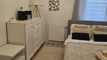 Een slaapkamer met een bed, nachtkastjes, een kaptafel, een radiator, een kroonluchter en een raam met gordijnen.