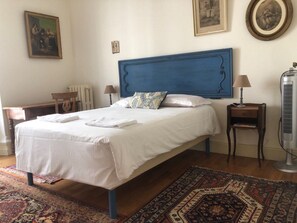 A bedroom with a large bed, a blue headboard, a bedside table with a lamp, a radiator, and a floor lamp.