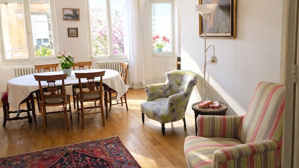 A dining area with a round table and chairs, a floral armchair, a striped sofa, and a patterned rug.