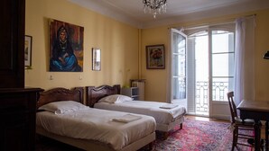A hotel room with two beds, a chandelier, a large window with a view, and a dining area.