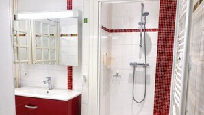 A bathroom with a white sink, red cabinet, mirror, and a shower area with red-tiled walls.