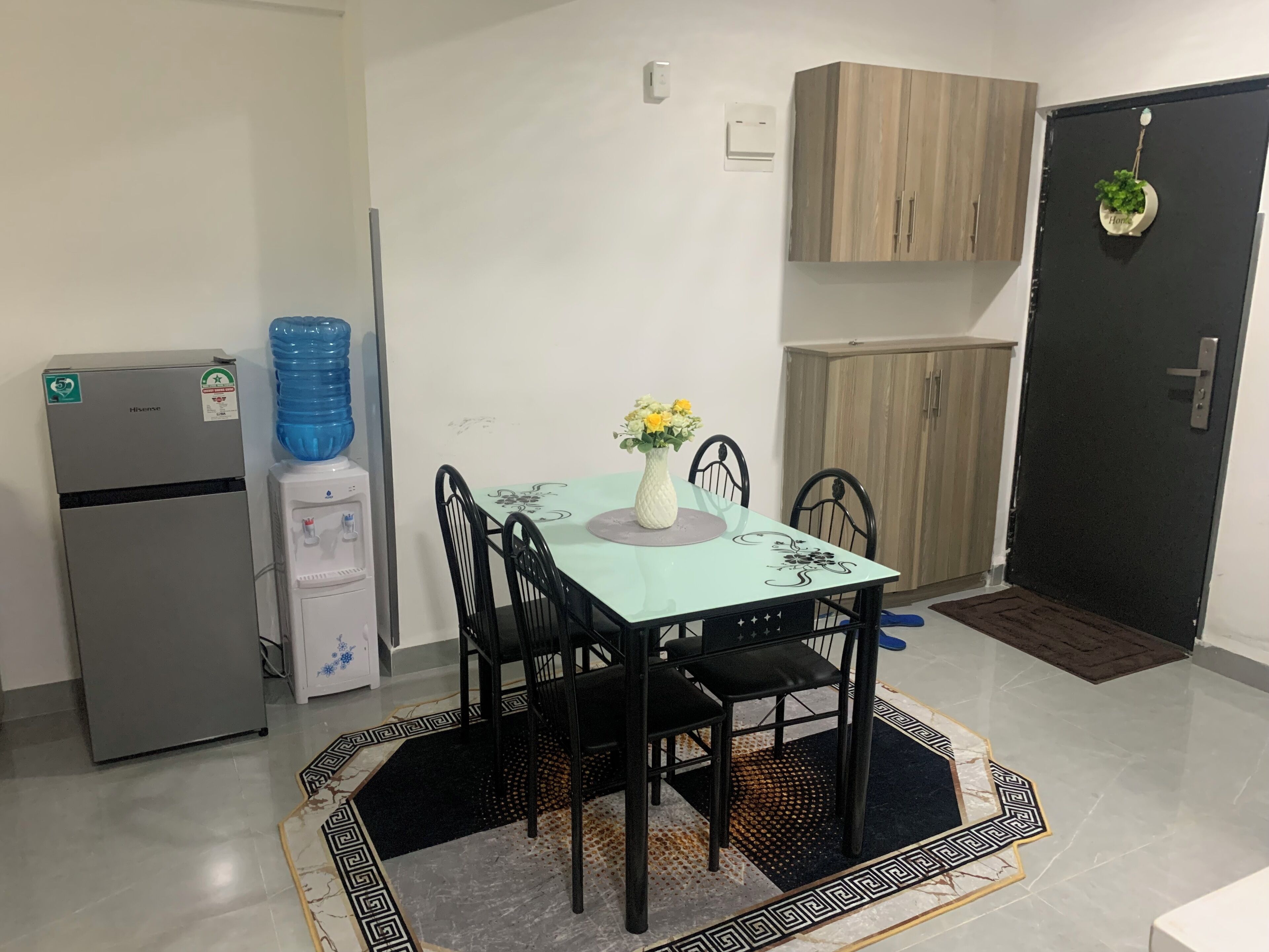 A compact kitchen with a refrigerator, water dispenser, and a dining table with chairs.