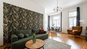 A modern living room with a patterned wallpaper, a green sofa, a round coffee table, a dining area, and a view of the city.