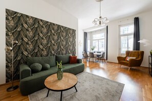 A modern living room with a patterned wallpaper, a green sofa, a round coffee table, a dining area, and a view of the city.