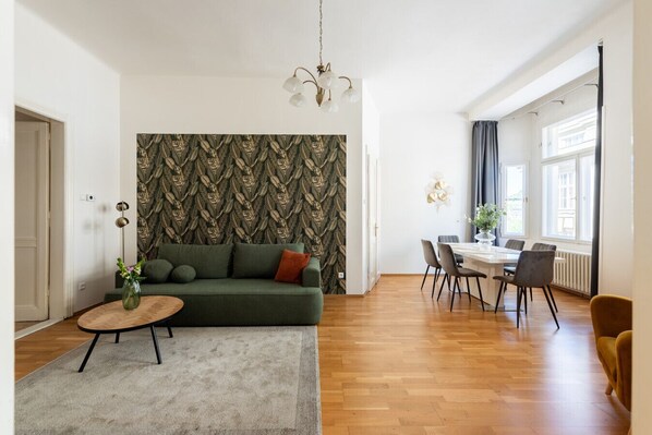 A modern living room with a sofa, a dining table, and a chandelier.