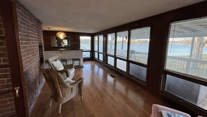 Una habitación amplia con pisos de madera, ventanas grandes, una silla de mimbre y una pequeña mesa.