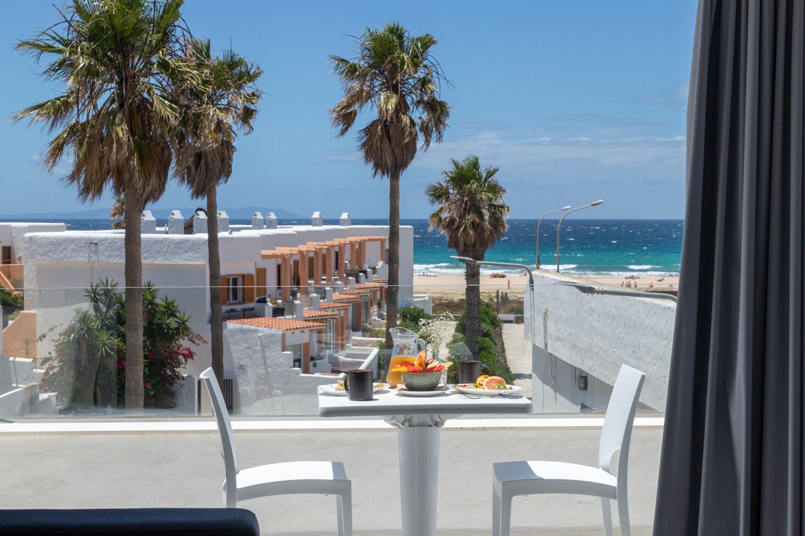 A balcony with a table set for breakfast overlooking a beach.