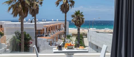 A balcony with a table set for breakfast overlooking a beach.