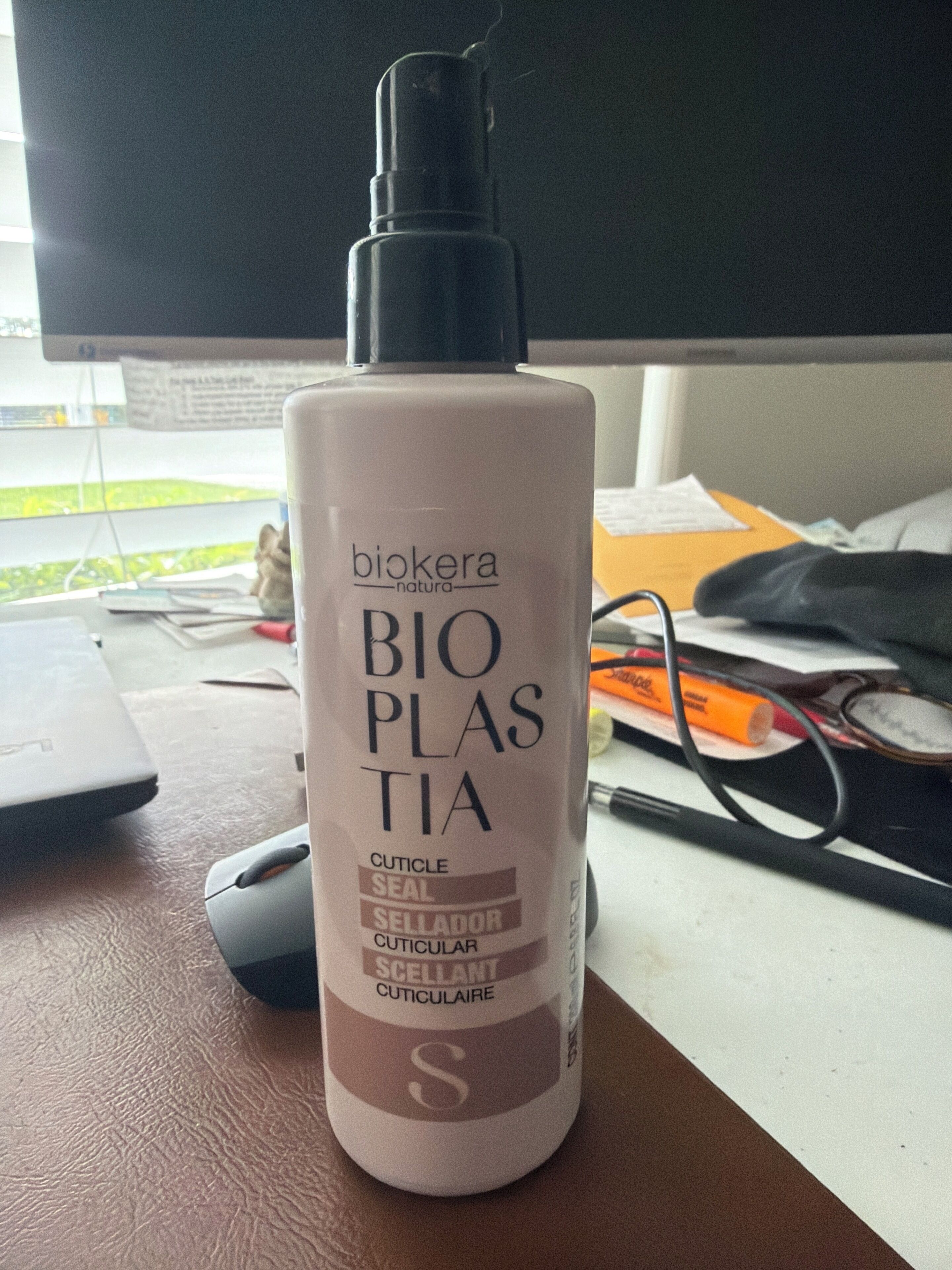 Una botella de Biokera Natura Bio Plastia sobre un escritorio con un monitor de computadora, un teclado y algunos papeles.