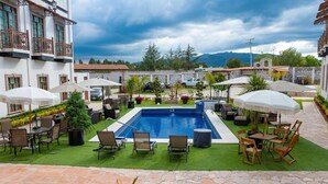 Un espace piscine doté d’une piscine rectangulaire, entourée de chaises longues et de parasols, aménagé sur une pelouse artificielle, avec une terrasse en pierre au premier plan.