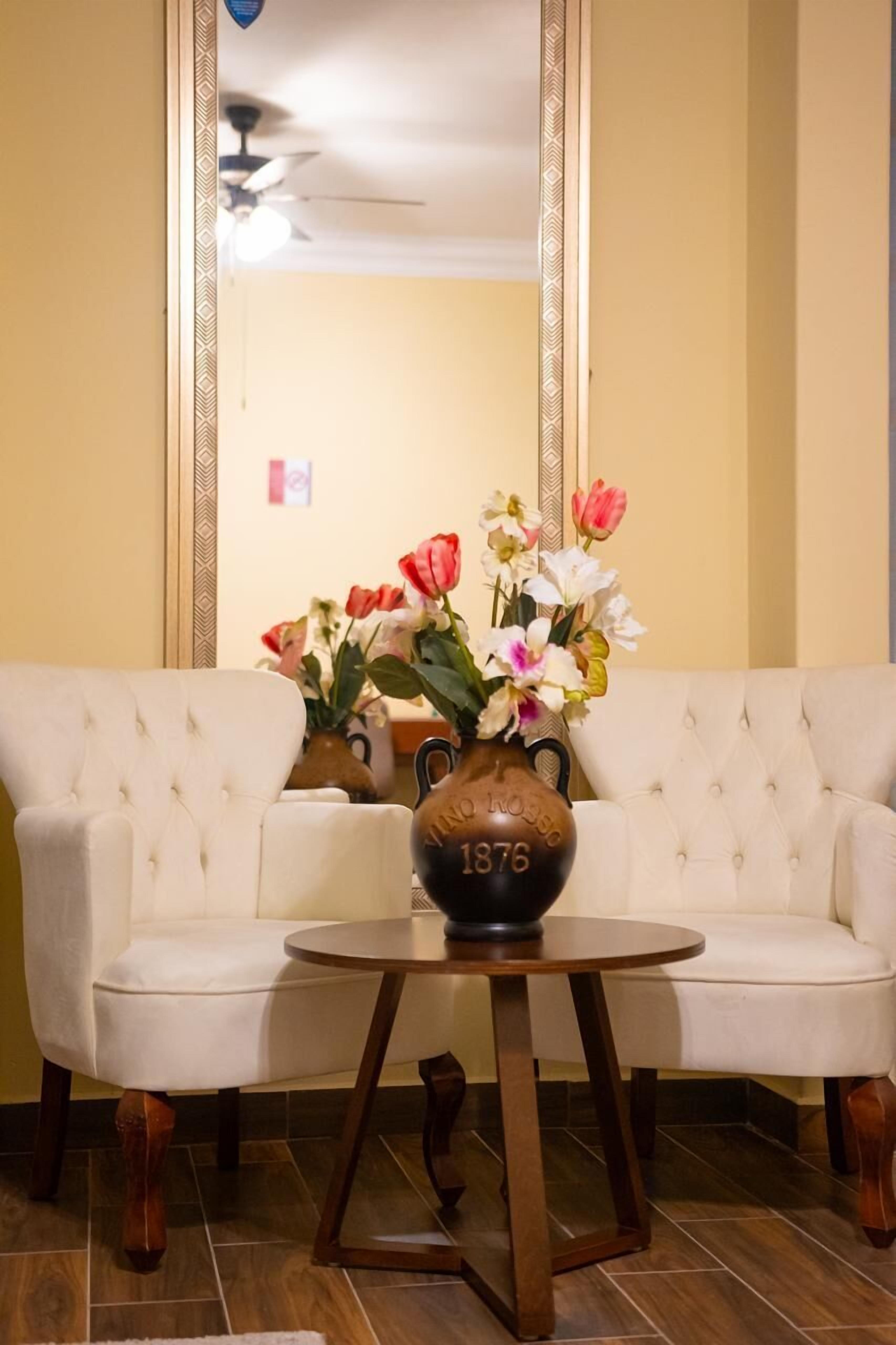 Una habitación con un sofá blanco, una mesa redonda de madera y un florero con flores.