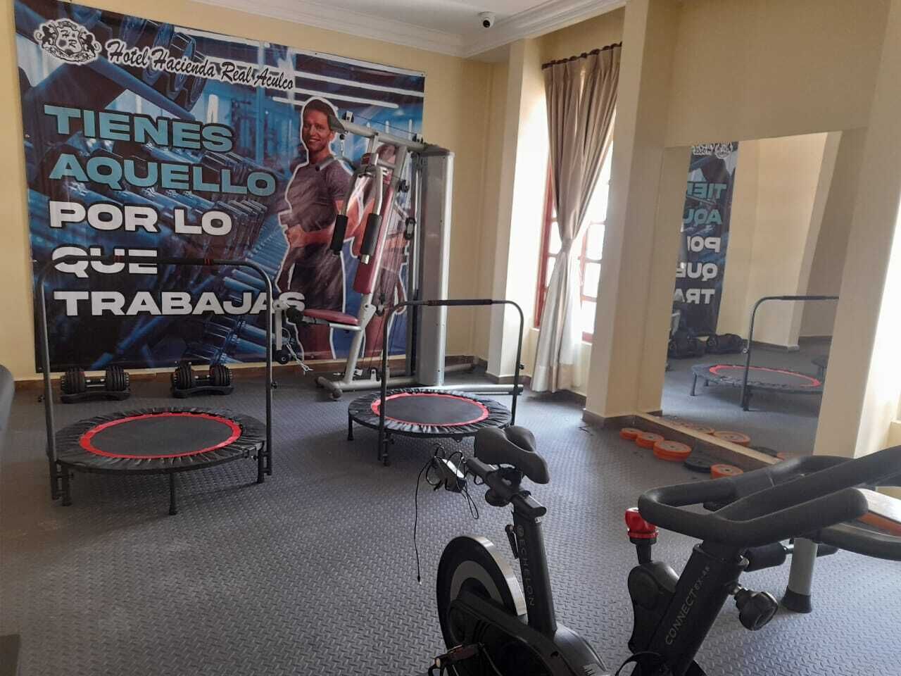 A gym with exercise equipment including a stationary bike, a trampoline, and a weight bench.