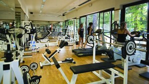 Une salle de sport équipée de divers appareils d’exercice, dotée de grandes fenêtres et d’un plancher en bois.