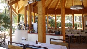 Un pavillon extérieur en bois, doté de tables et de chaises, d’un espace bar et d’un toit de chaume.