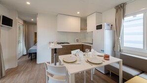 Une petite cuisine équipée d’un four à micro-ondes, d’un réfrigérateur et d’une cuisinière. On y trouve également un coin repas avec une table pour deux personnes, des chaises blanches et un canapé.