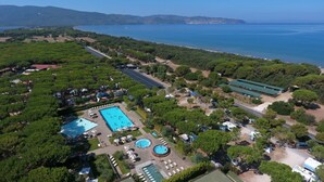 An aerial view of a resort with multiple swimming pools, a road, and surrounding greenery.