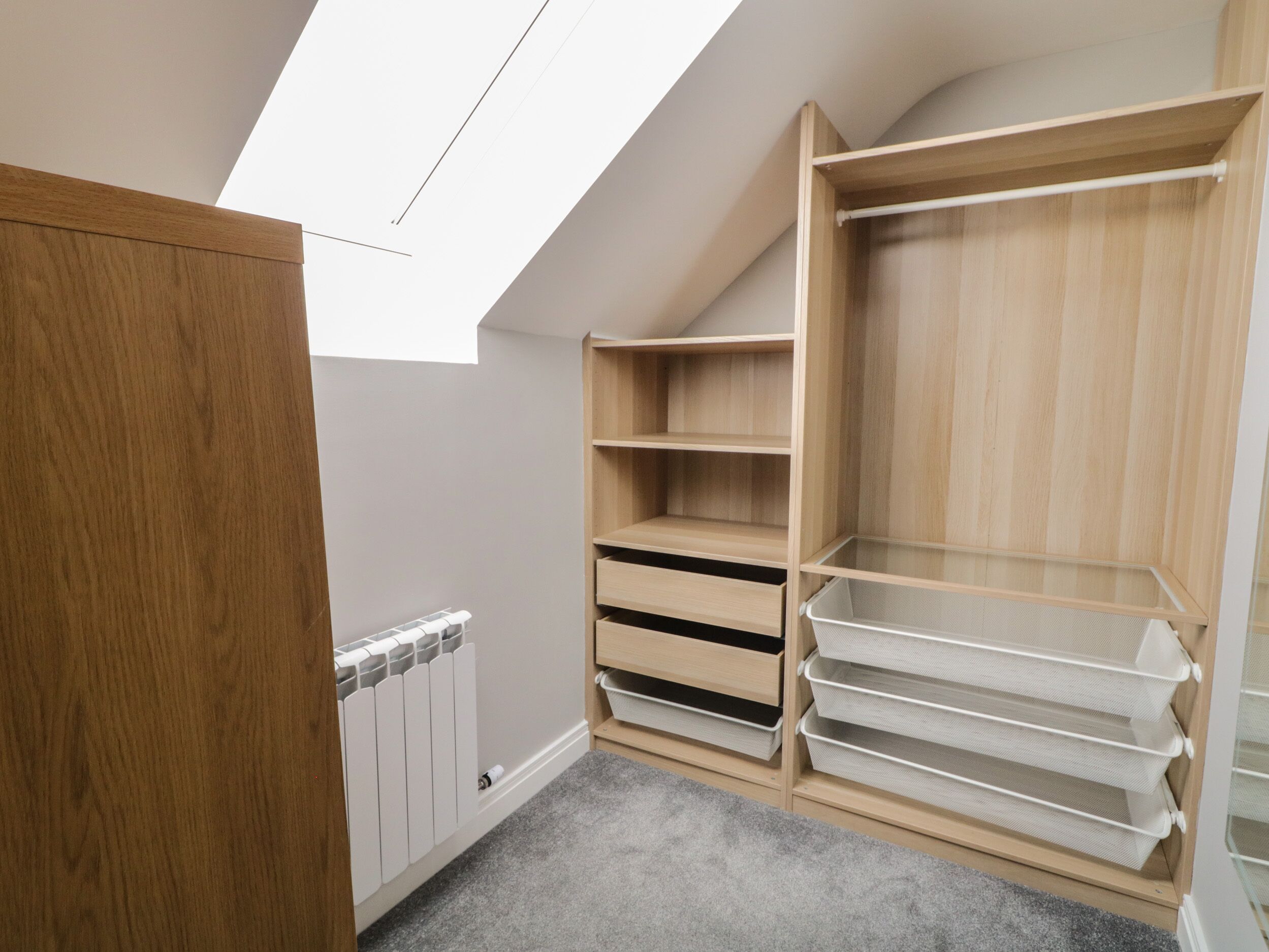 A room with a sloped ceiling, wooden shelving, and a radiator.