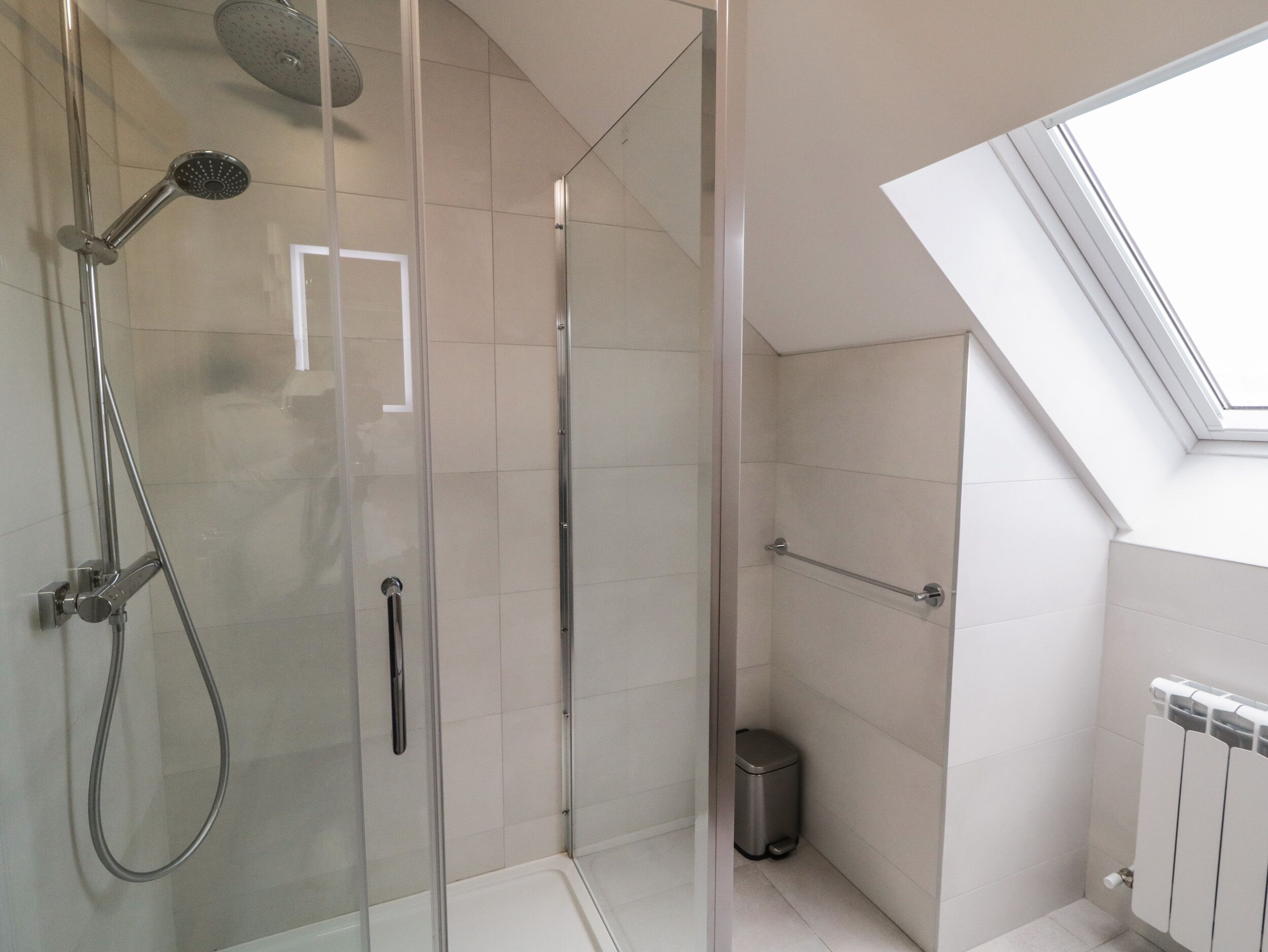 Un área de ducha moderna con puerta de vidrio, ducha de mano y ducha de lluvia vertical.