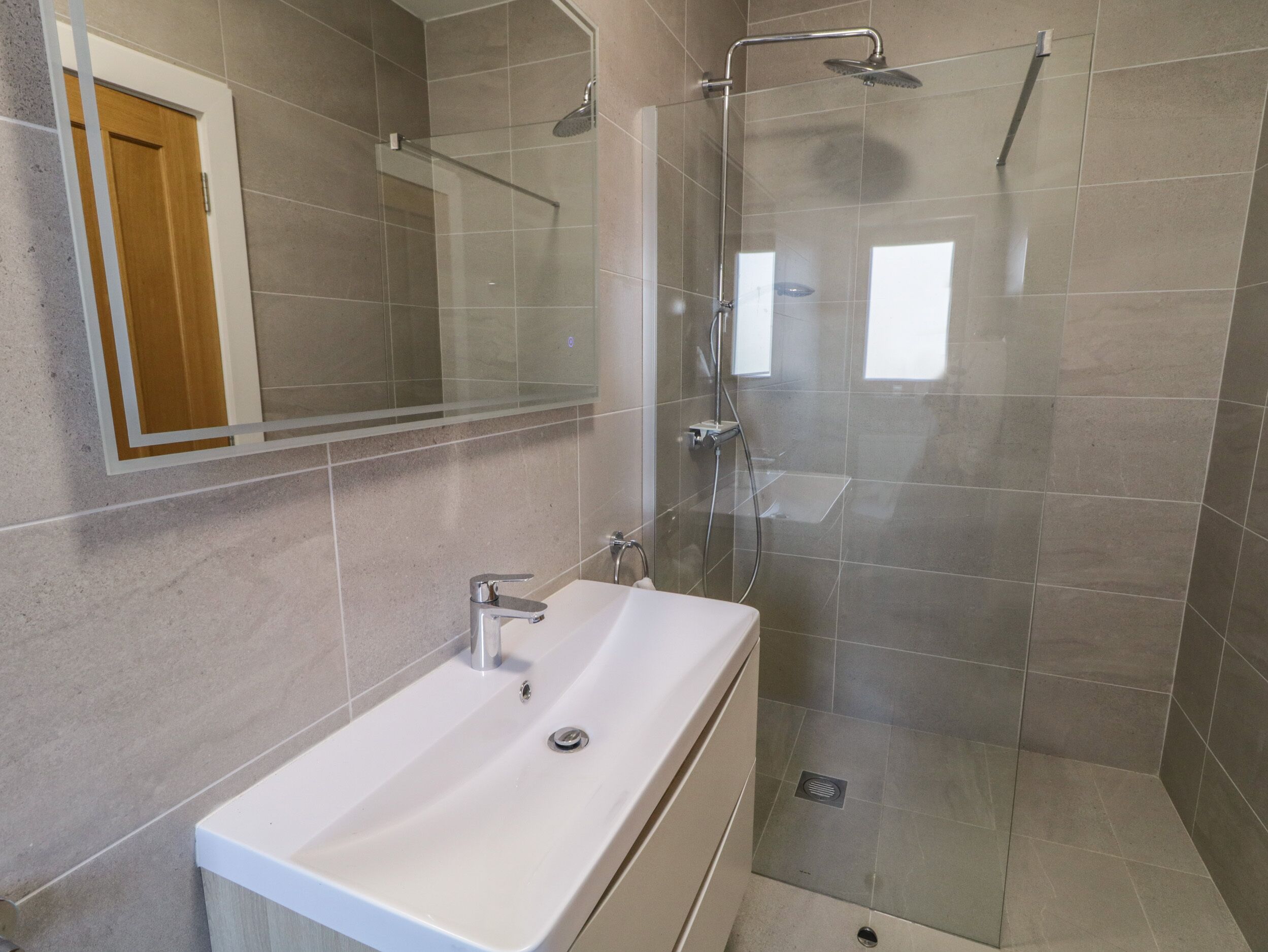A modern bathroom with a glass shower enclosure, a white sink, and a mirror.