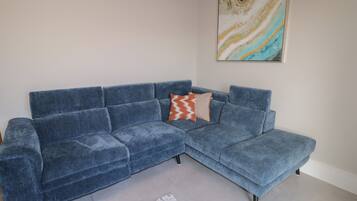 A blue sectional sofa with a patterned throw pillow, a blue rug, and a marble wall art piece.